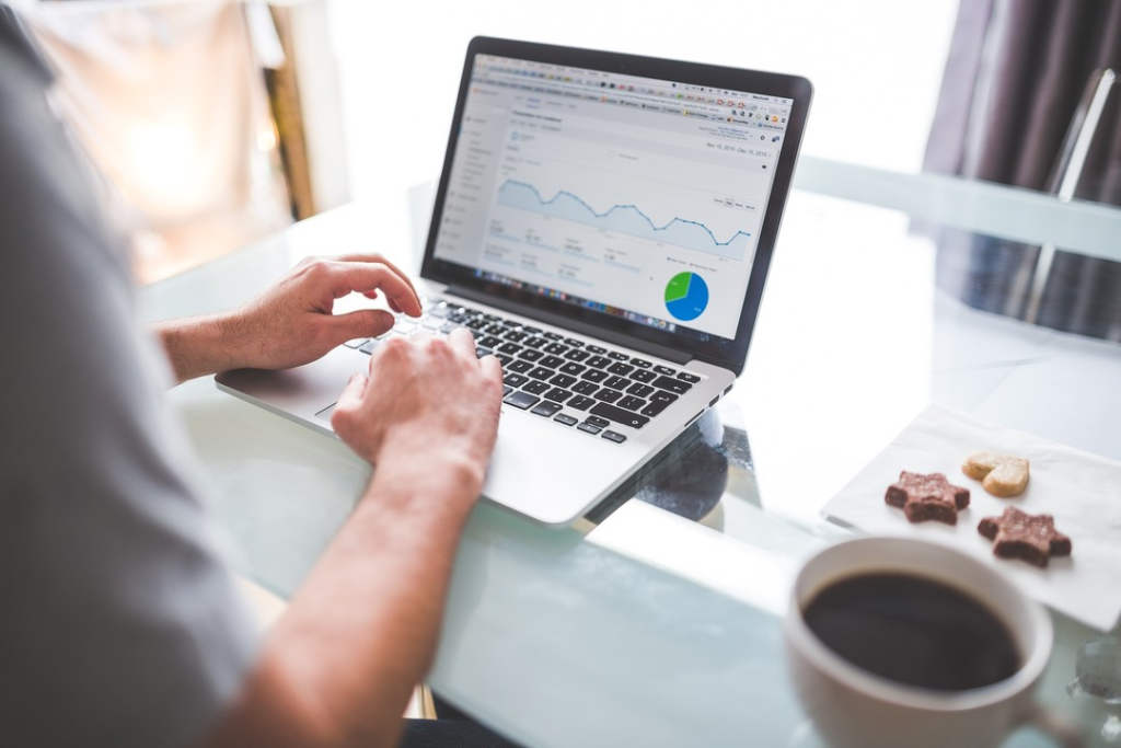 A marketer reviewing website analytics and performance charts on a laptop, coffee in hand, analyzing data before scaling ad spend.