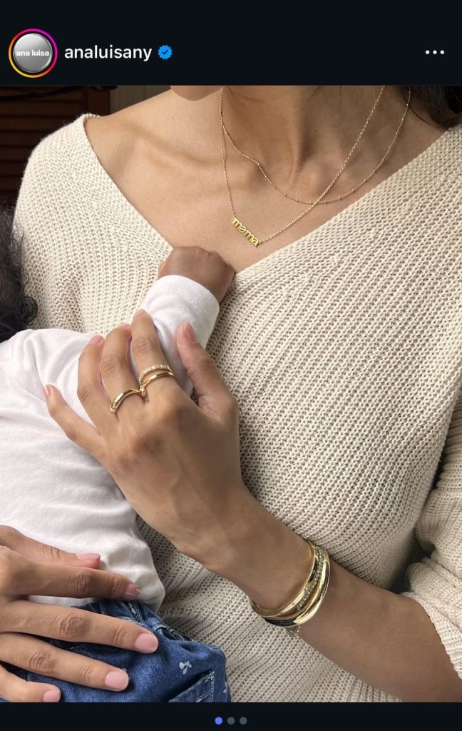 Ana Luisa Instagram ad featuring a mother wearing a "mama" necklace and stacked gold rings while holding her child.