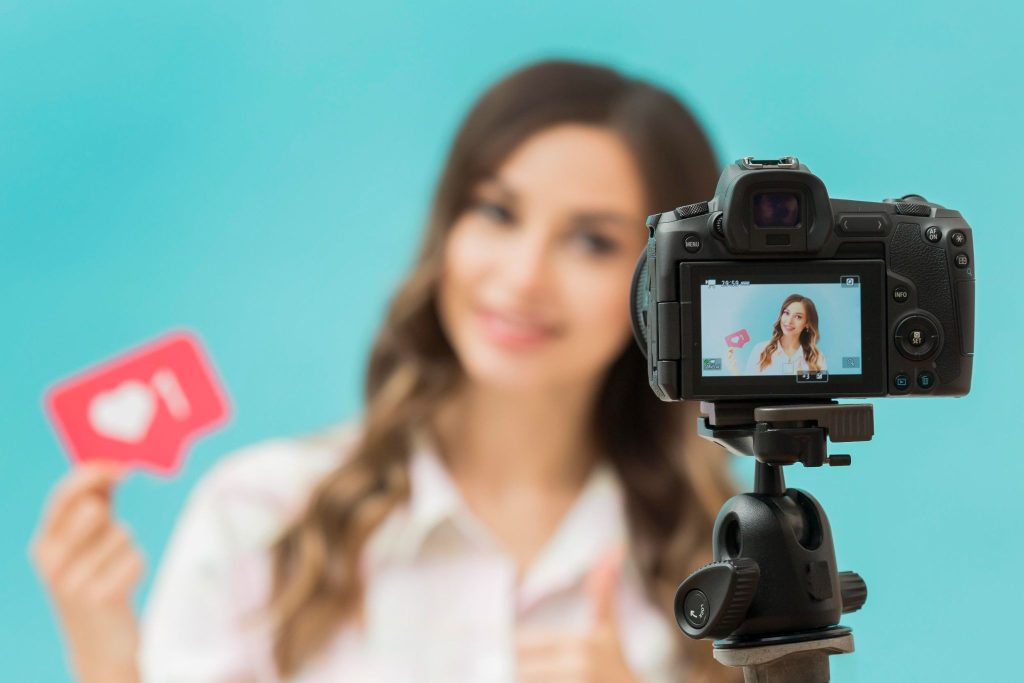 Woman holding a like-button prop while filming a phone-style UGC weight loss Facebook ad on a tripod camera.