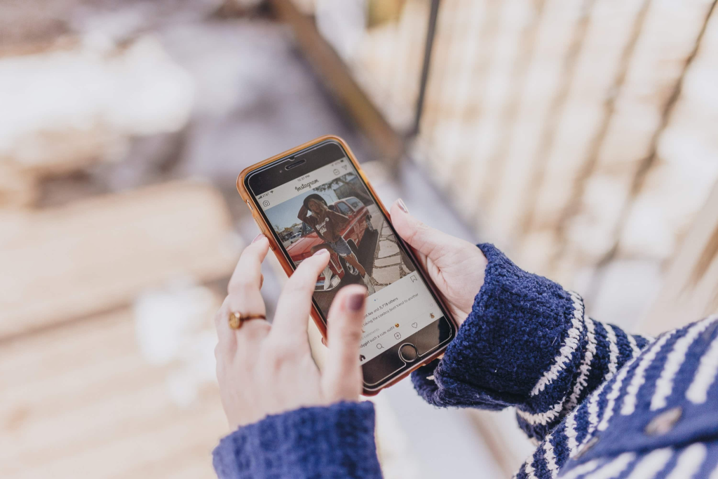 Shopper in a striped sweater scrolling Instagram on an iPhone, viewing the kind of mobile feed where Dynamic Product Ads appear.