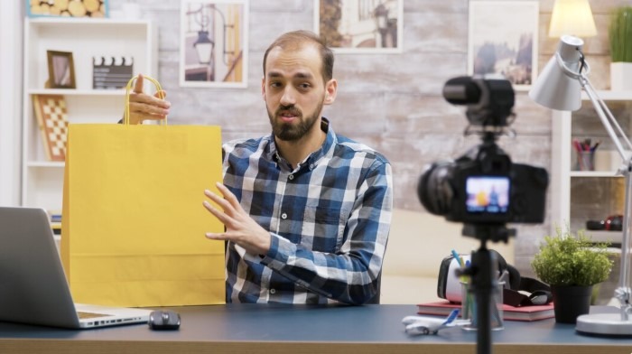 Male creator filming a product video at his desk while holding a yellow shopping bag.