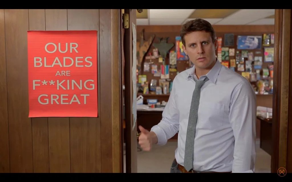 Dollar Shave Club's 2012 launch video showing founder Mike Dubin standing next to the iconic "Our Blades Are F**KING Great" poster in the warehouse office.