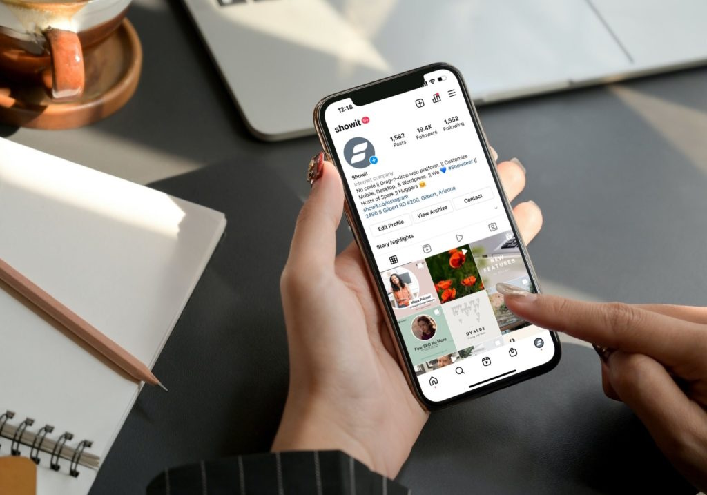 Hand holding a smartphone displaying the Showit Instagram profile, with a finger tapping to engage with Story highlights.