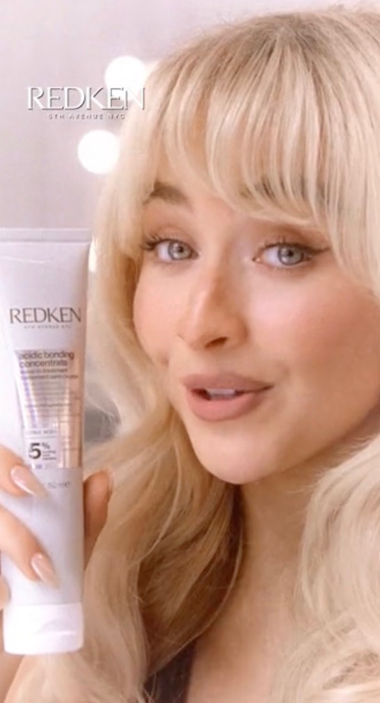 Blonde woman holds a Redken Acidic Bonding Concentrate tube beside her face, brand logo overlaid.