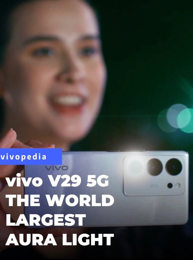 Smiling woman holds a silver vivo V29 5G phone showing its camera and Aura Light. "vivopedia" label visible.