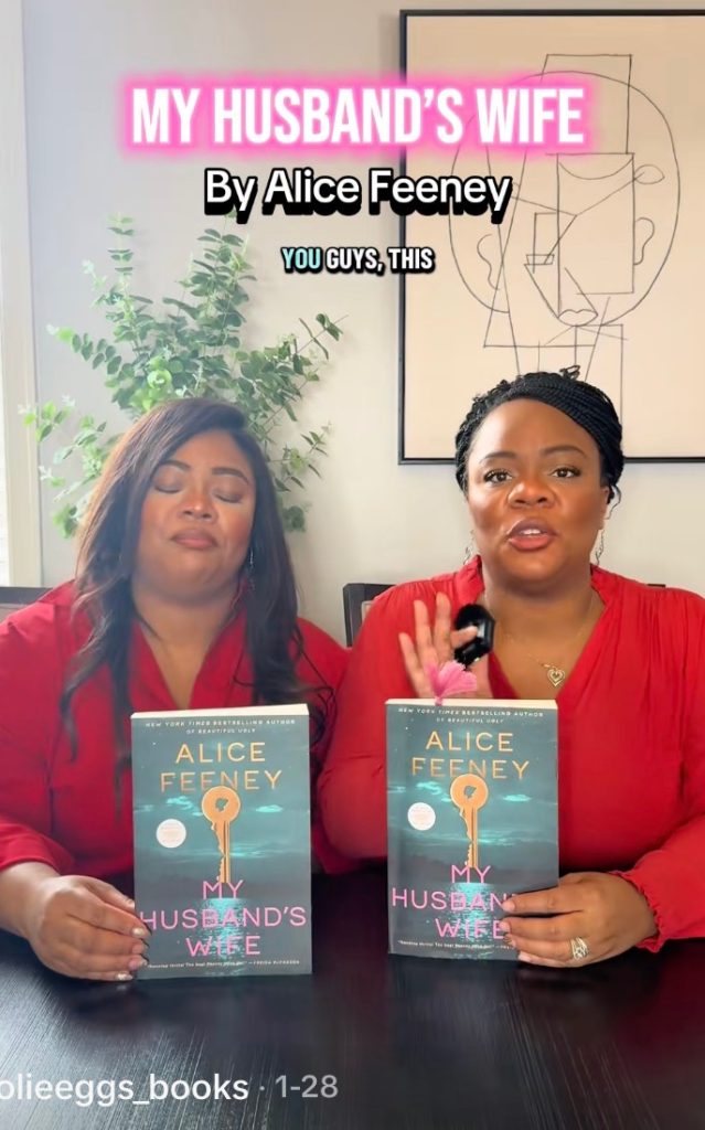 Two women in red hold up copies of Alice Feeney's thriller "My Husband's Wife."