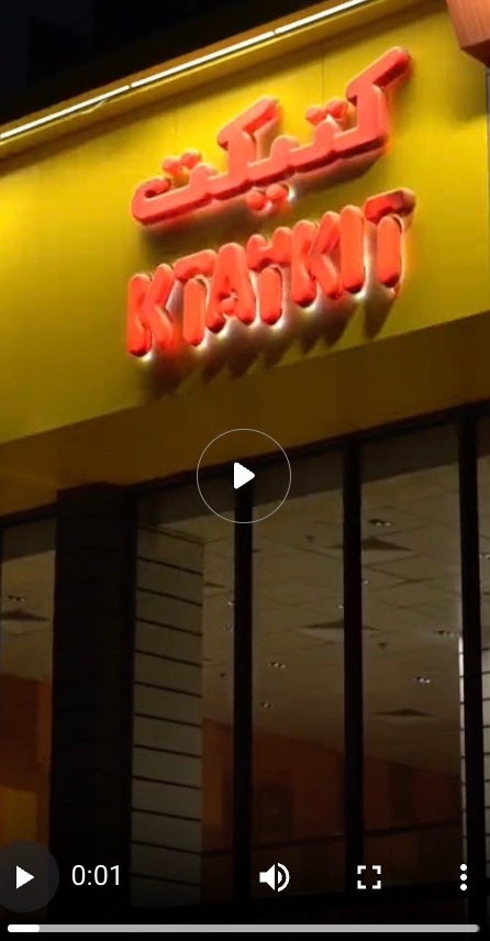 Video still of KTAYKIT restaurant's illuminated orange storefront sign in Arabic and English at night.