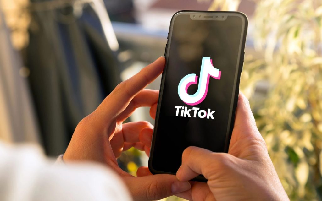 Person holding a smartphone displaying the TikTok logo and app name on a black screen.