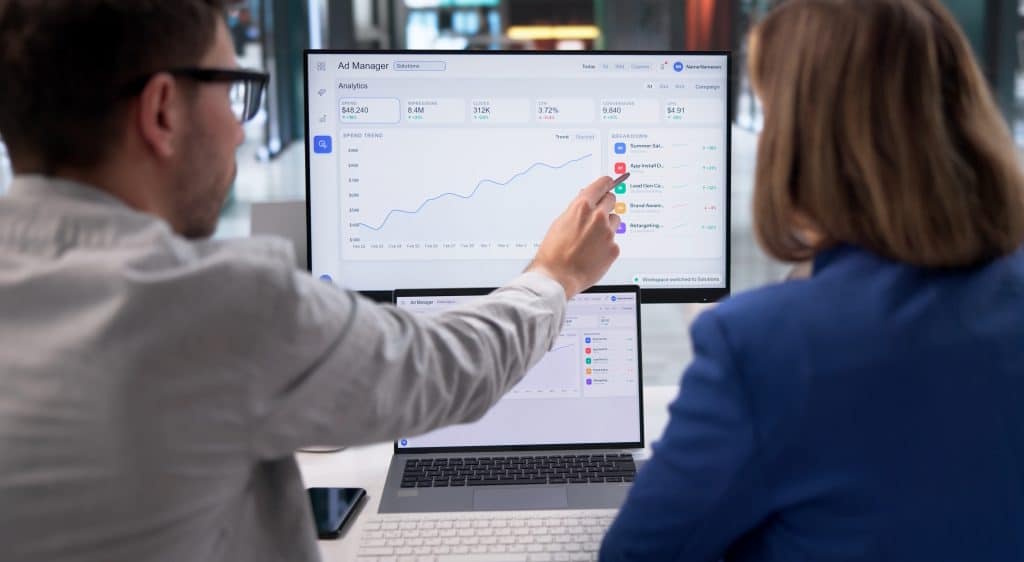 Two marketers reviewing Ad Manager analytics and spend trends on a laptop screen.
