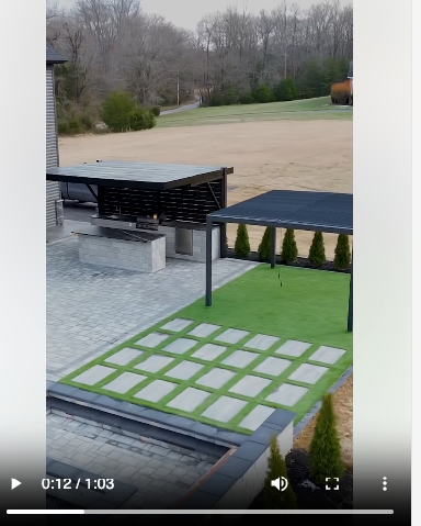 Still from a hardscaping project, showing an overview of a yard and a green area.